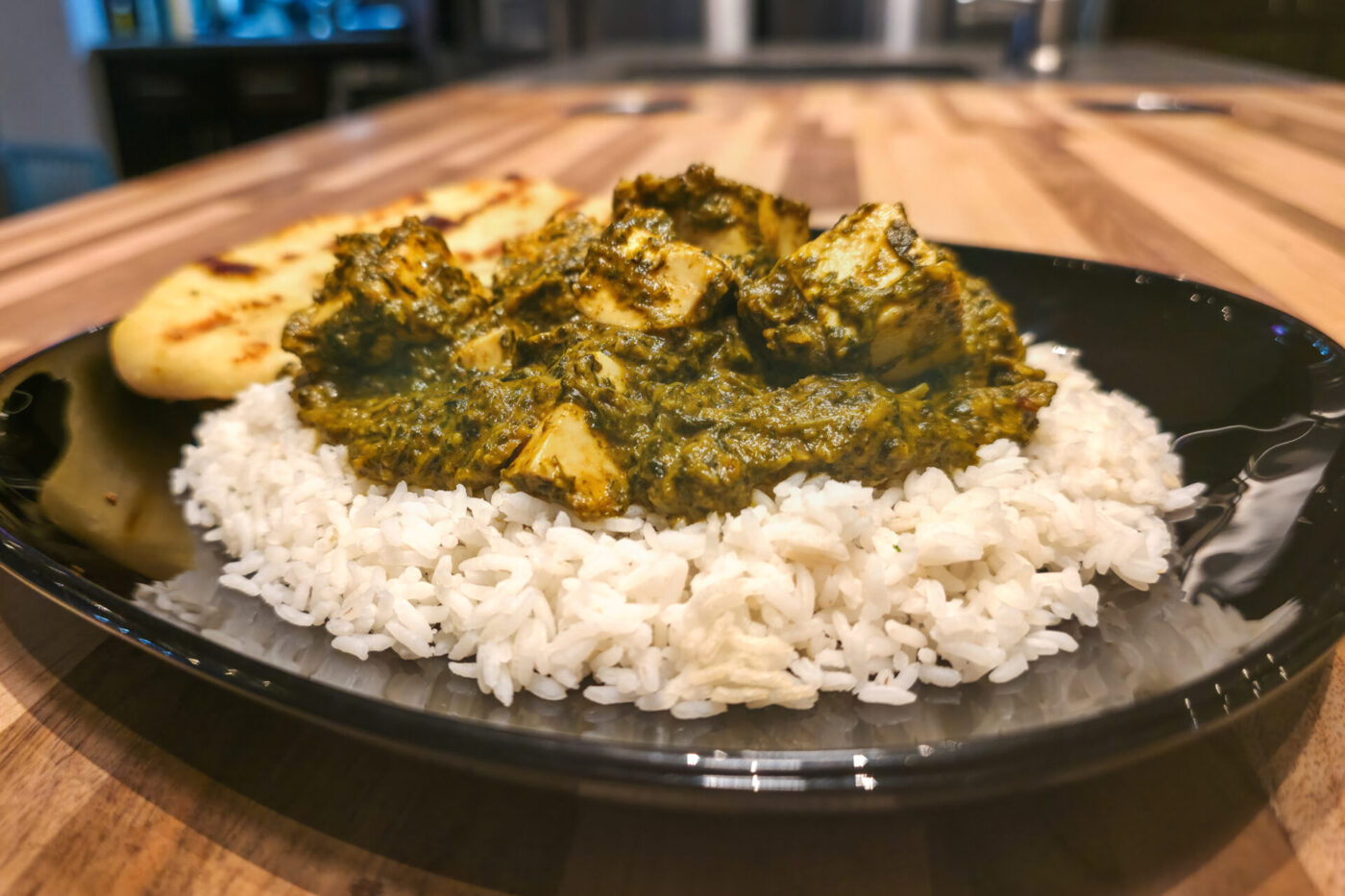 Spinach Palak Paneer with diced paneer cubes in green curry, served over rice with grilled flatbread.