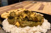Spinach Palak Paneer with cubed paneer over rice, grilled flatbread on a black plate