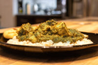 Spinach Palak Paneer with cubed paneer over rice on a black plate, flatbread at the edge.