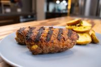 Grilled čevapčiči sausages with char marks beside roasted potato wedges on a grey plate