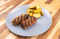 Two grilled Čevapčiči Sausages With Cheese with char lines, served with roasted potato slices on a gray plate