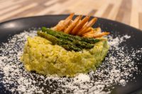 Plated Asparagus Risotto with Shrimp topped with grilled asparagus spears, dusted with parmesan on a black plate.