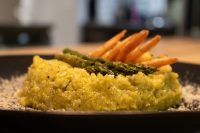Yellow Asparagus Risotto with Shrimp topped with grilled asparagus spears and curled shrimp on a dark plate.