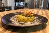 Black plate of Asparagus Risotto with Shrimp topped with asparagus tips and curled fried shrimp, dusted with parmesan.