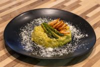 Plated Asparagus Risotto with Shrimp: yellow risotto topped with asparagus spears and shrimp on a black dish.