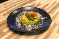 Plated Asparagus Risotto with Shrimp topped with grilled shrimp and asparagus on a black dish.