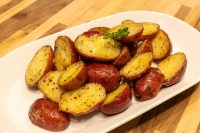 Halved Baby Red Potatoes with Butter, skins and gold flesh showing, on a white oval plate