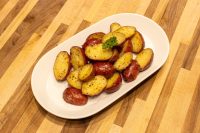 Halved Baby Red Potatoes with Butter, golden and glossy, garnished with parsley on a white oval plate.