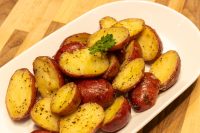 Halved red and gold potatoes glossed with butter and pepper, garnished with parsley on a white oval plate
