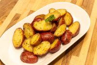 Halved Baby Red Potatoes with Butter, golden and glossy, on a white oval platter with parsley.