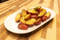 Halved red potatoes glazed in butter with pepper flecks, plated on a white oval dish on a wooden table.