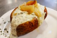 Baked Potato with Herb Sour Cream, split open on a white plate and topped with creamy herb sauce and pale golden slices.