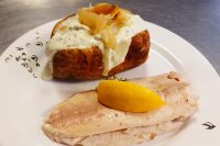 Baked Potato with Herb Sour Cream topped with onions, served beside a poached fish fillet and lemon slice.