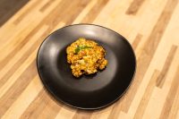 Golden-brown Buffalo Cauliflower Steak on a black plate, garnished with a small herb leaf.