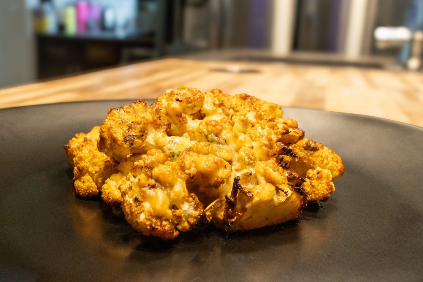 Roasted Buffalo Cauliflower Steak with charred edges and crumbled cheese on a black plate.