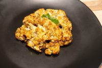 Roasted Buffalo Cauliflower Steak with melted cheese and charred edges on a black plate.