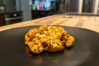 Roasted Buffalo Cauliflower Steak with crispy golden-brown edges on a black plate over a wood counter.