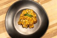 Roasted Buffalo Cauliflower Steak with charred golden-orange florets, garnished with fresh herb, on a dark plate.
