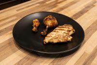 Grilled Lemon and Garlic Chicken breast and two drumsticks on a black plate, wooden counter