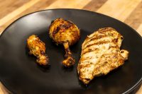 Grilled Lemon and Garlic Chicken breast and two drumsticks with char marks on a black plate