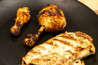 Grilled Lemon and Garlic Chicken drumsticks and breast piece with char marks on a black plate.
