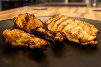 Grilled Lemon and Garlic Chicken drumsticks and a breast portion with charred skin on a dark plate.