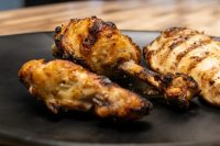 Grilled Lemon and Garlic Chicken drumsticks and a piece with char marks on a dark plate