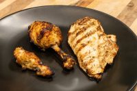 Grilled Lemon and Garlic Chicken drumstick, wing, and breast with char marks on a black plate