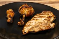 Grilled Lemon and Garlic Chicken breast and two drumsticks with char marks on a black plate