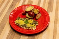 Pesto Chicken Breasts topped with herbed cheese, plated with roasted potato halves on a red dish.