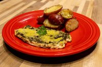 Pesto Chicken Breasts topped with green herb coating and parmesan, served with roasted potato halves on a red plate