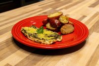 Pesto Chicken Breasts with green herb coating, parsley garnish, and roasted red potatoes on a red plate