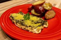 Pesto Chicken Breasts topped with grated parmesan and parsley, served with roasted red potatoes on a red plate.