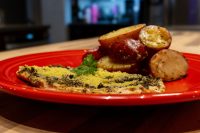 Pesto Chicken Breasts with a green herb-and-cheese crust on a red plate, parsley garnish, roasted potatoes beside it.