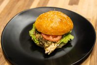 Pesto Chicken Sandwich with Parmesan on a sesame bun with tomato and lettuce, on a black plate.