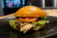 Pesto Chicken Sandwich with Parmesan on a sesame bun with tomato and lettuce, skewer on top