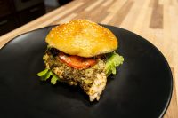 Pesto Chicken Sandwich with Parmesan on a sesame bun with tomato and lettuce, served on a black plate.