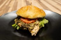 Pesto Chicken Sandwich with Parmesan on a sesame bun with tomato and lettuce, on a black plate.