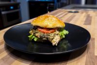 Pesto Chicken Sandwich with Parmesan on a sesame bun with lettuce and tomato on a black plate
