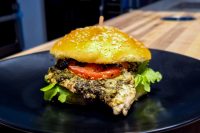 Pesto Chicken Sandwich with Parmesan on a sesame bun with tomato and lettuce, served on a black plate.