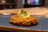 Tuna Cakes A single breaded, fried Tuna Cake on a dark blue plate, garnished with a lemon slice and parsley.