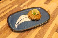 Tuna Cakes Golden breaded Tuna Cake topped with a lemon slice and herb sprig, served with a creamy sauce swoosh.