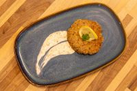 Tuna Cakes Golden Tuna Cakes patty topped with lemon and herb, served with creamy sauce on a blue plate.