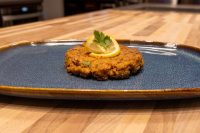 Tuna Cakes A browned Tuna Cake topped with a lemon slice and parsley on a dark blue plate.