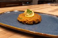 Tuna Cakes A golden-brown Tuna Cake topped with a lemon slice and parsley sprig on a blue ceramic plate.