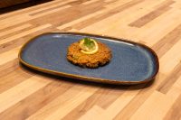 Tuna Cakes A fried Tuna Cake topped with a lemon slice and herb garnish, served on a blue oval plate.