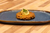 Plated Tuna Cakes A fried Tuna Cake on a dark blue plate, garnished with a lemon slice and parsley sprig.