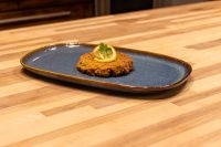 Tuna Cakes Golden fried Tuna Cake topped with a lemon slice and herb sprig on a blue oval plate.
