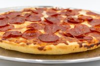 Close-up of 60 min. Pan Pizza with thick crust and overlapping pepperoni slices on a metal tray.