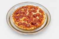 Overhead view of a 60 min. Pan Pizza topped with pepperoni and melted cheese on a round metal plate.